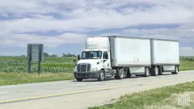 A white day cab pulling two white LTL trailers on highway