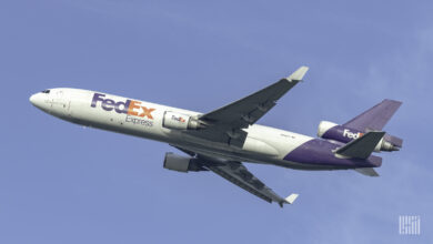 A purple-tailed FedEx plane crosses the blue sky.