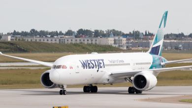 A jet with teal accents and WestJet logo rolls on a runway.