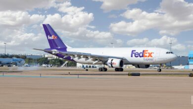 A purple-tail FedEx jet lands on a bright day with puffy clouds.