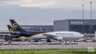 Two brown-tail UPS planes at an airport, with American Airlines hangars in the background.