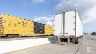 A tractor-trailer on a highaway next to a boxcar on a railroad