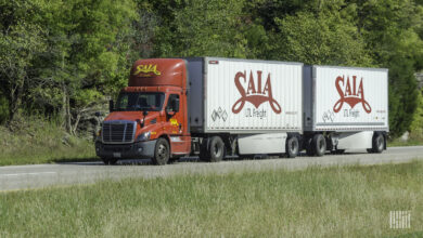 A red Saia tractor pulling two white Saia LTL trailers on highway