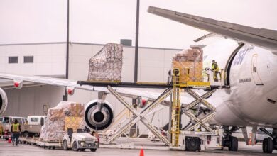 Close up from behind the wing of a cargo aircraft and a hydraulic lift loading a pallet through the side door.