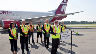 Speakers and onlookers wearing yellow safety vests in front of large jet to announce a new project.