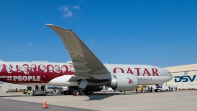 A side view of a Qatar Airways Cargo freighter jet in front of a DSV cargo warehouse.
