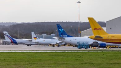 Cargo jets, including a yellow DHL plane, in a row at an airport.