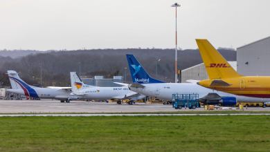 Cargo jets, including a yellow DHL plane, in a row at an airport.
