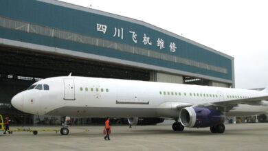 A white freighter jet with windows blocked out in front of a Chinese repair hangar.