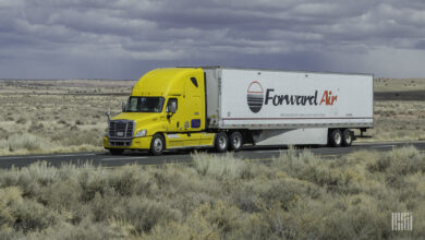 A Yellow tractor pulling a white Forward Air dry van trailer on a highway