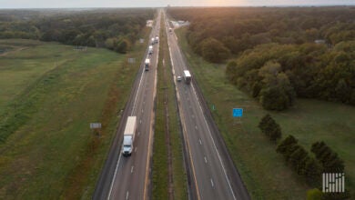 Trucks and cars drive on a roadway surrounded by green foliage.