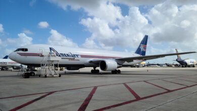 A blue-tailed Amerijet aircraft sits on the tarmac under a sunny sky with white clouds.