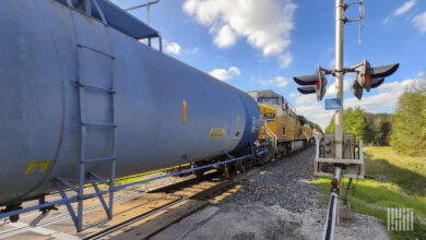 A freight locomotive pulls tank cars through a rail crossing.