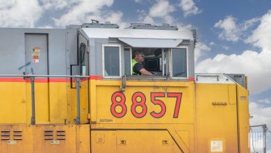A man sits inside a freight train locomotive.
