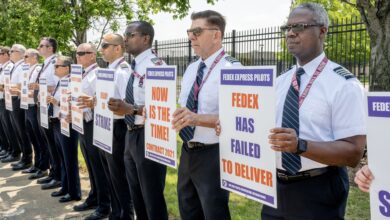 FedEx pilots in white, short-sleeve shirts stand side-by-side holding signs to protest FedEx's contract negotiations.