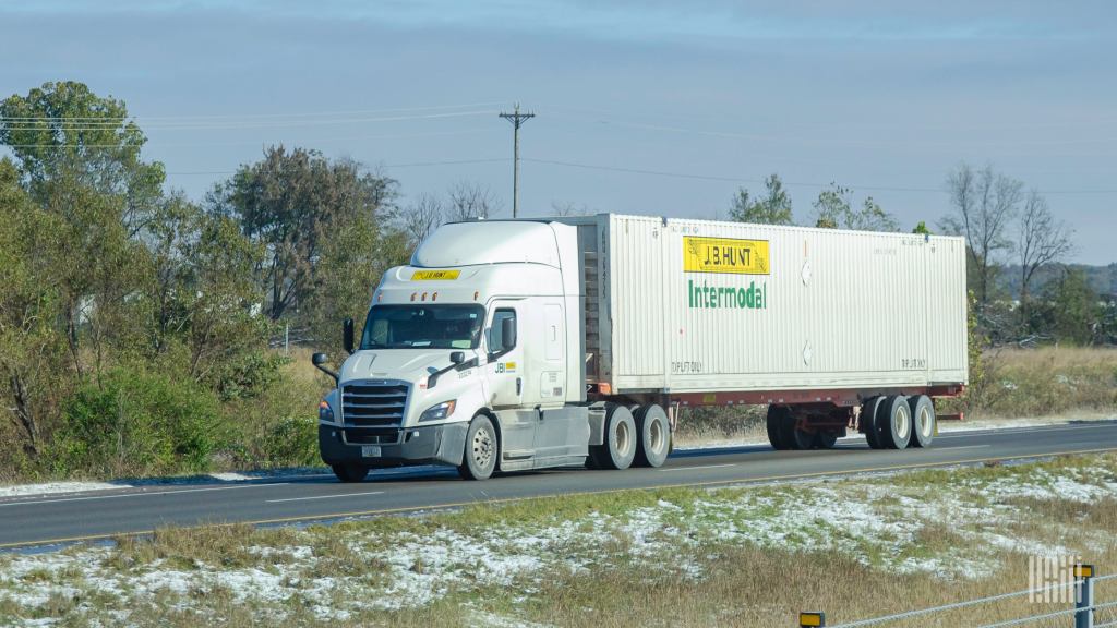 A white J.B. Hunt tractor pulling a J.B. Hunt intermodal container on a highway