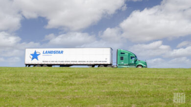 A green tractor pulling a white Landstar trailer