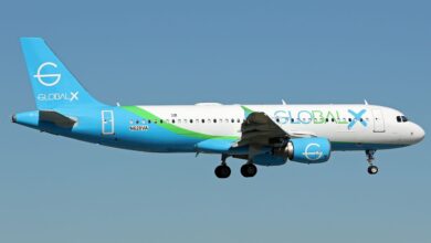 A Global Crossing Airlines passenger jet, with light blue and green trim approaches airport on a clear day.