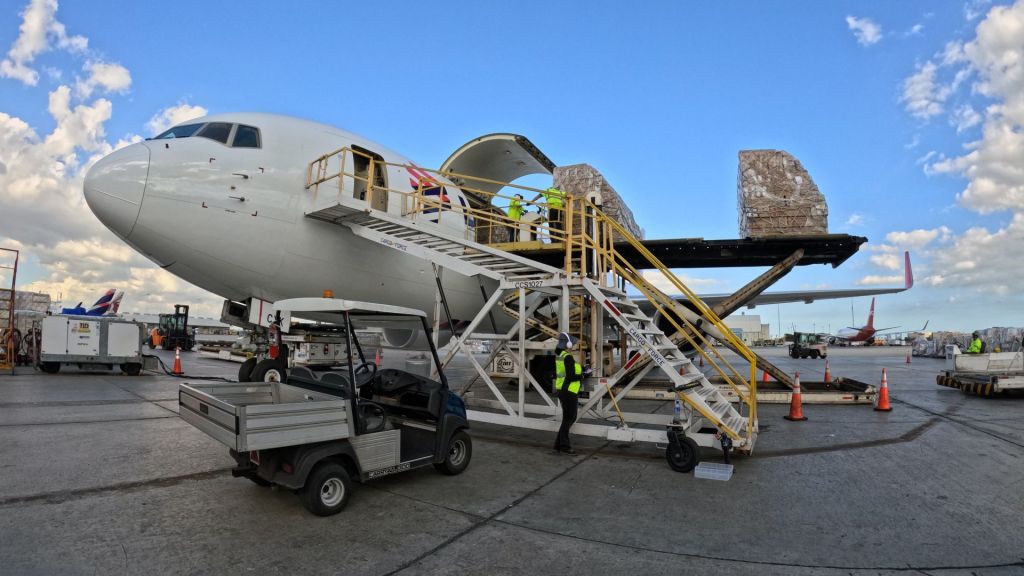 A cargo container on a large lift being loaded on a white cargo jet.