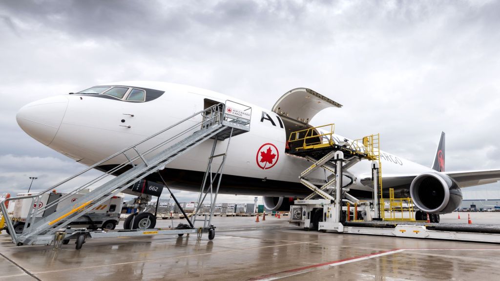 An Air Canada cargo jet with black underbelly gets loaded through side door.
