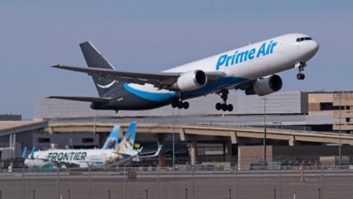 A dark-and-light blue Amazon cargo jet takes off from an airport.