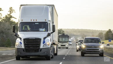 White semi-truck driving on a road with passenger cars in the next lane