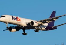 A purple-tailed FedEx plane approaches landing with wheels down.