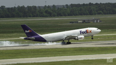 A purple-tail FedEx plane creates a puff of smoke when its tires touch down on the runway.