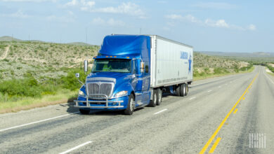 A blue tractor pulling a Landstar trailer on a highway