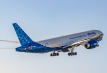 Blue/white Silk Way West Airlines cargo jet rises into the sky. View from the rear.