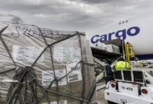 A large pallet of freight covered in plastic and straps on the tarmac next to a large cargo plane.