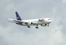 A purple-tail FedEx jet with wheels down on approach to an airport.