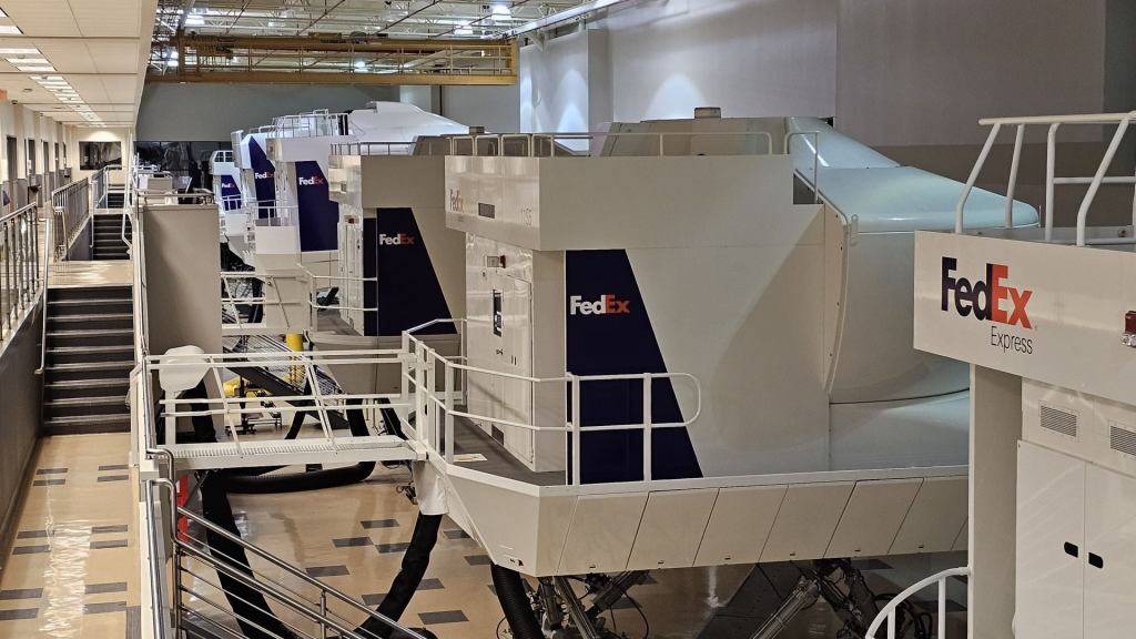 A bank of white and purple FedEx flight simulators in a building.