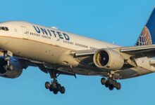 A blue-tailed United Airlines jet approaches runway with wheels down.