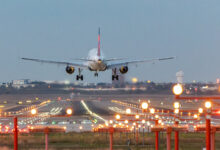 View from behind a commercial jet as it prepares to touch down on lighted runway at dusk.