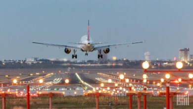 View from behind a commercial jet as it prepares to touch down on lighted runway at dusk.
