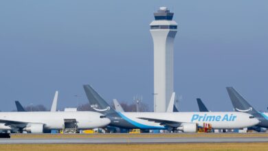 Amazon Prime Air freighters with blue accents on the tarmac underneath tall air traffic control tower.