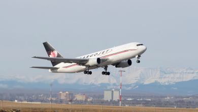 A blue-tailed Cargojet aircraft takes off with snow-covered mountains in the background.