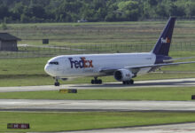 A purple-tailed FedEx cargo jet on a taxiway with grass fields around it.