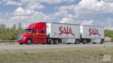 A red Saia tractor pulling two Saia pup trailers on a highway