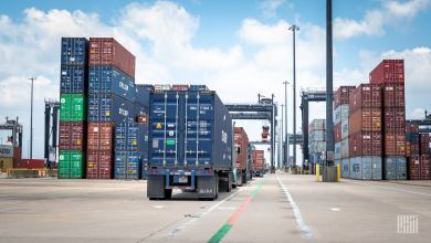 Image shows containers, container trcuks, sky.