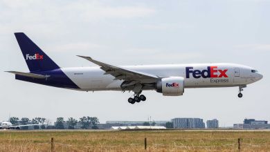 A purple-tail FedEx jet with wheels down for runway landing.