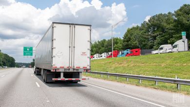 A trailer being pulled on a highway and tractors parked at a rest stop