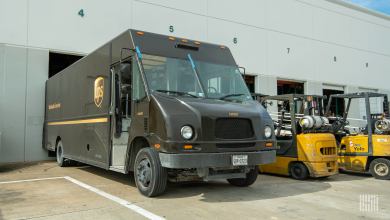 A UPS package van is backed up to a warehouse door with forklifts parked to its side.