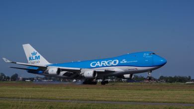 A medium-blue KLM Cargo jumbo jet lands on the runway on a sunny day.