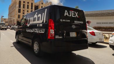 A black delivery van with Ajex Logistics logo driving in the city on a sunny day.