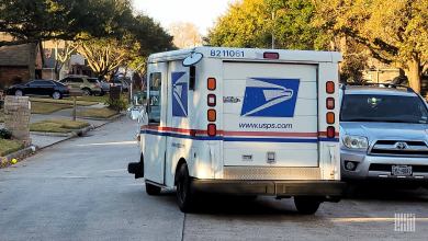 Rear view of a USPS mail van maneuvering on a neighborhood street.