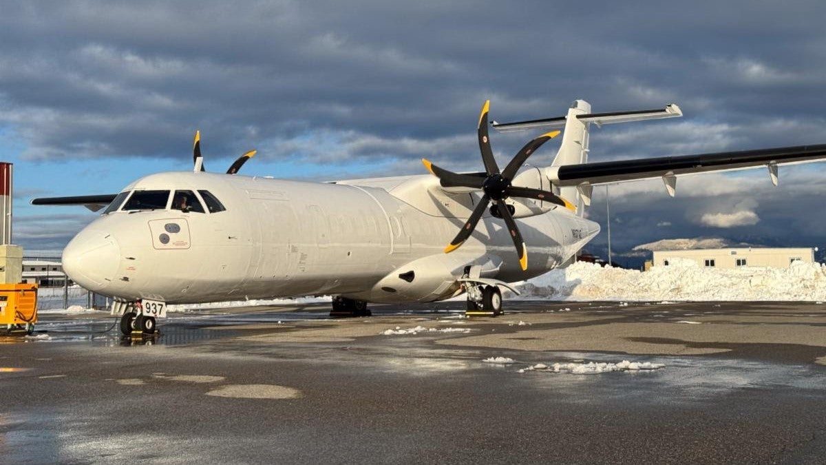 A white, twin-turboprop plane sits on the tarmac.