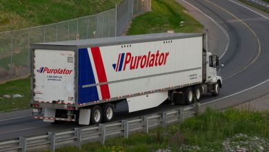 A Purolator semi-truck with blue and red lettering drives on a curvy road.