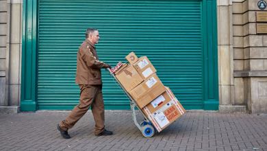 A parcel driver walks with a handtruck carrying packages.